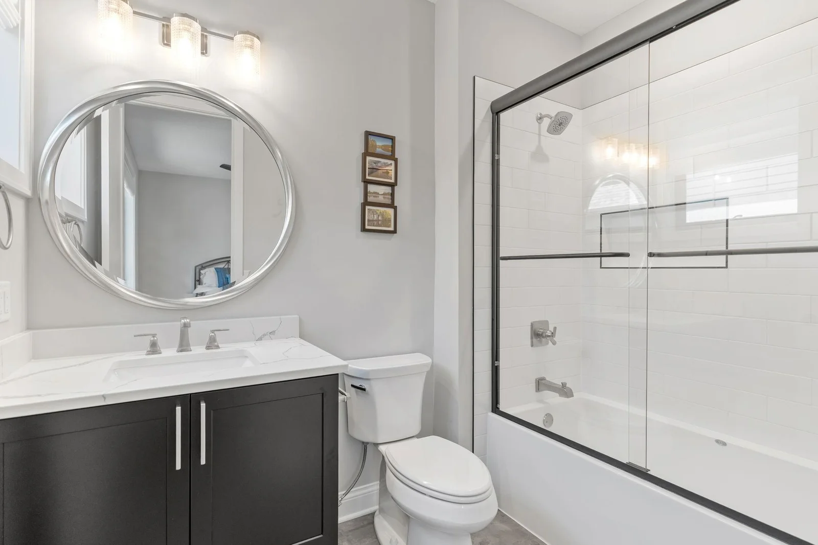 Private full bathroom features enameled vanity cabinet with quartz countertop and the tub features subway tile surround , shampoo niche and glass doors