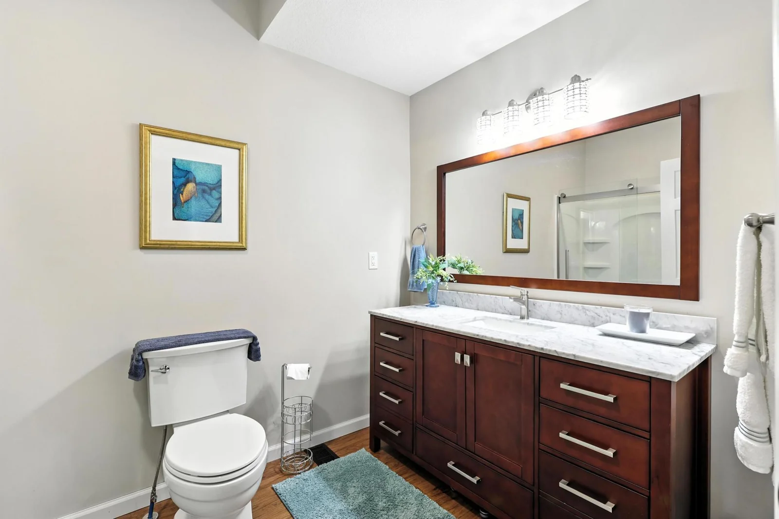 Sleek and modern, the second bathroom features a wide marble vanity with dual sinks, contemporary lighting, and a large framed mirror. A walk-in shower with glass doors completes the space.