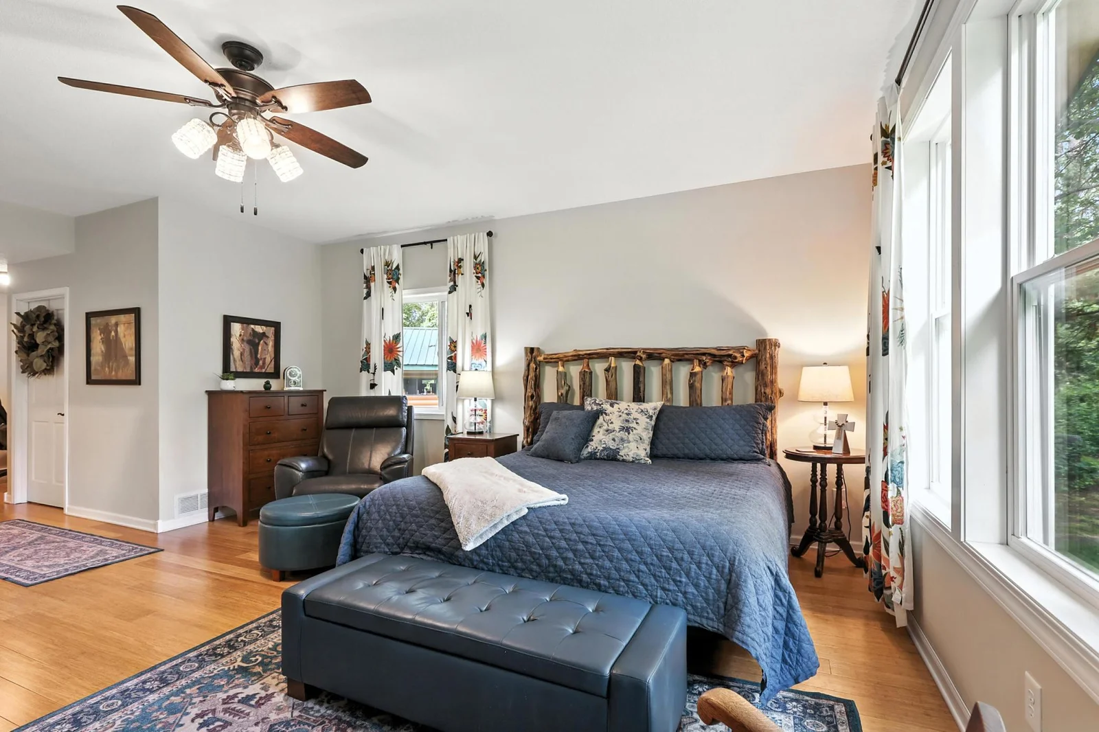 The spacious primary suite features oversized windows, hardwood floors, and a statement rustic log headboard. Plenty of natural light and a tranquil atmosphere make this a restful escape.