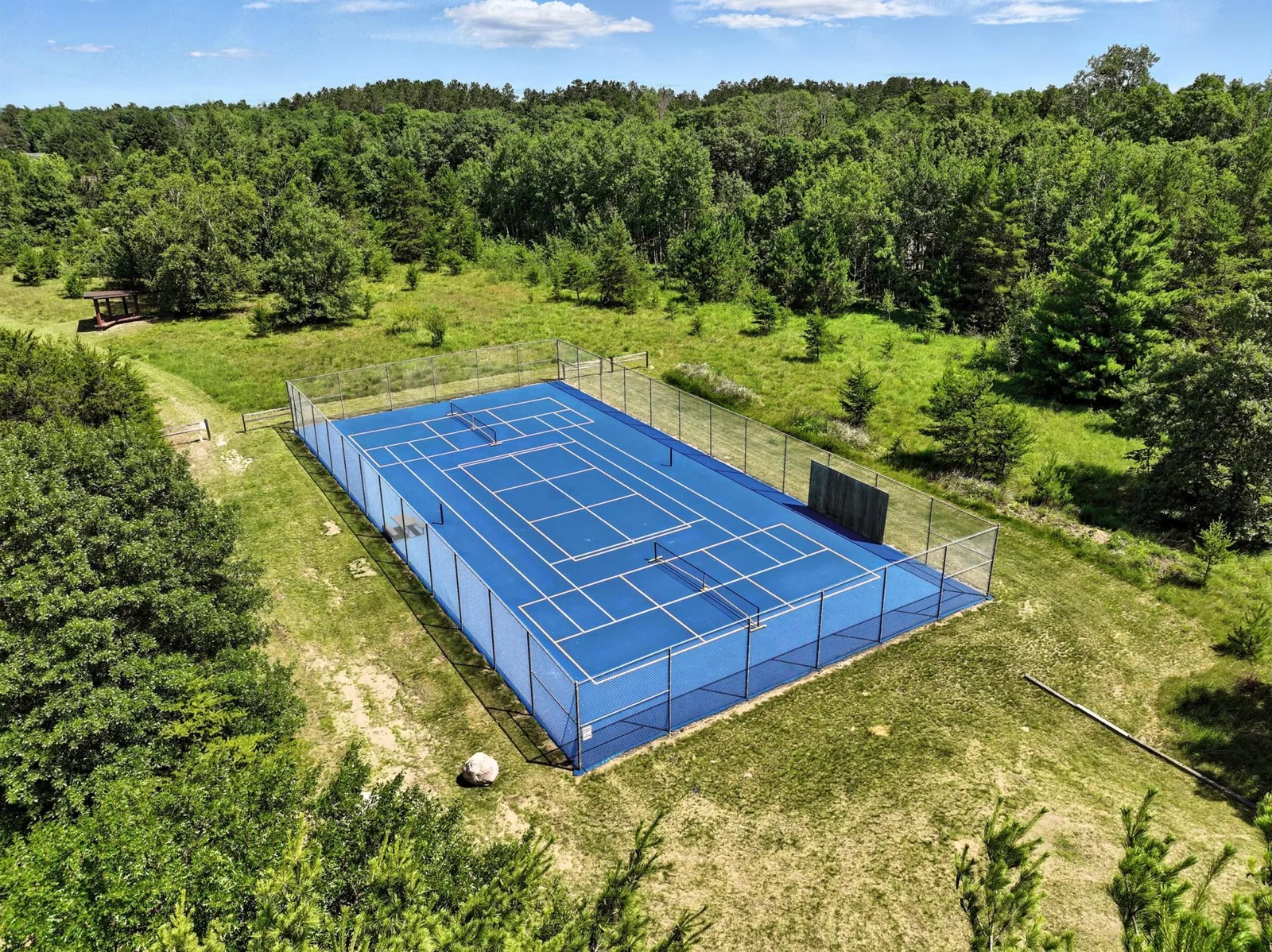 Well-maintained blue courts offer multiple layouts for tennis and pickleball amid a private wooded setting.
