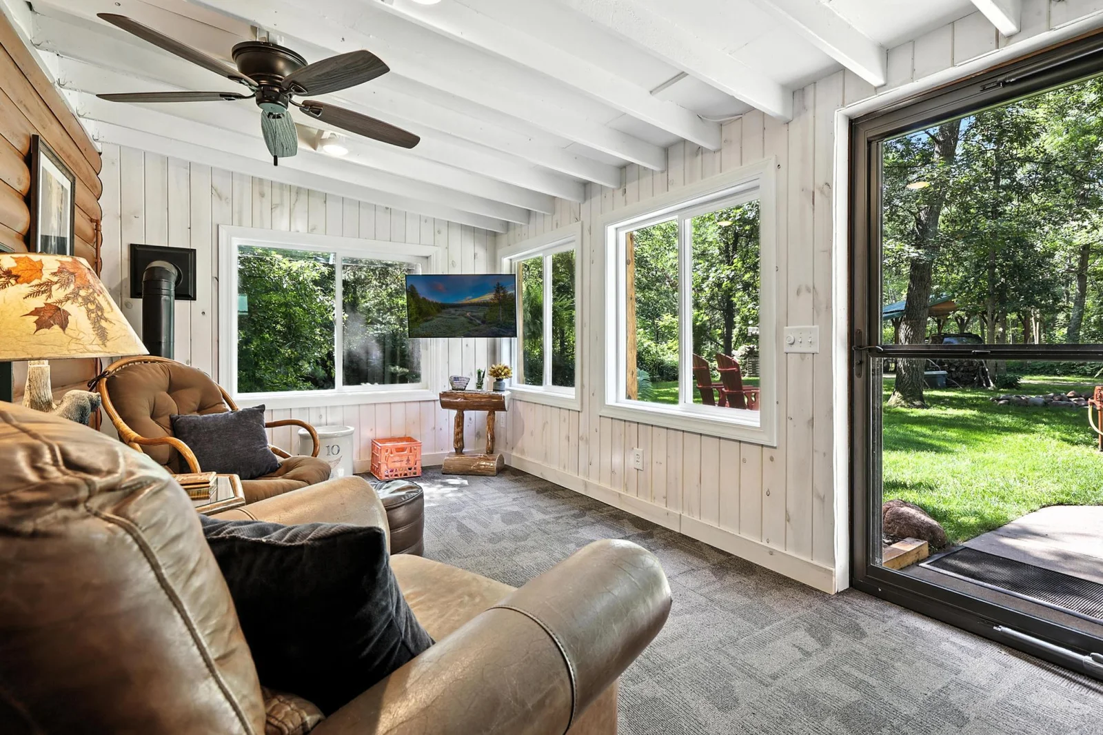 Expansive windows frame views of the lush backyard in this bright and airy four-season room, complete with wood stove, outdoor access, and comfortable lounging space.