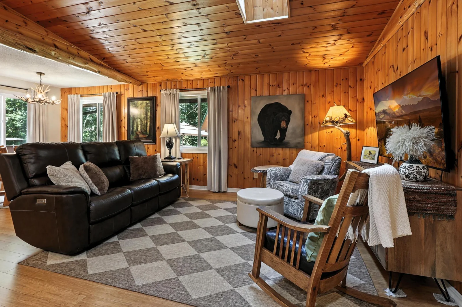 Spacious and inviting, the living room features wood-clad walls and ceilings, a skylight for added daylight, and plenty of seating. The room is grounded by a checkered area rug and anchored by cozy, lodge-inspired décor.