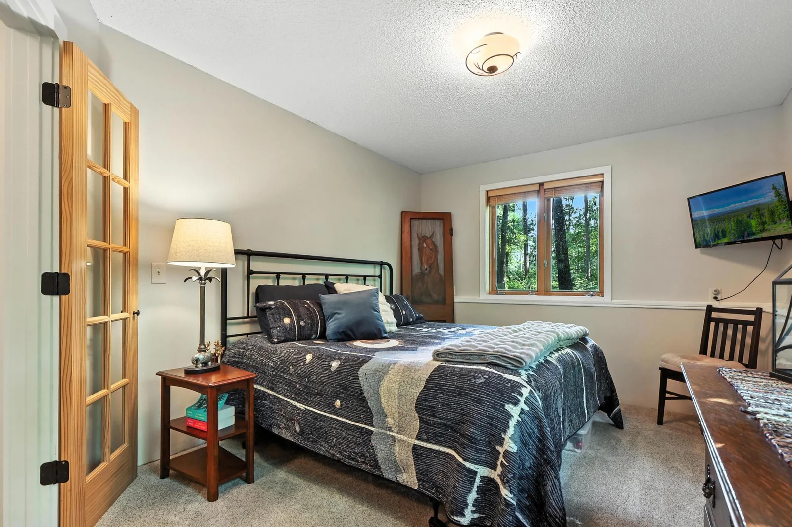 Bright and cozy room with a peaceful wooded view, French door entry, and space for restful nights.