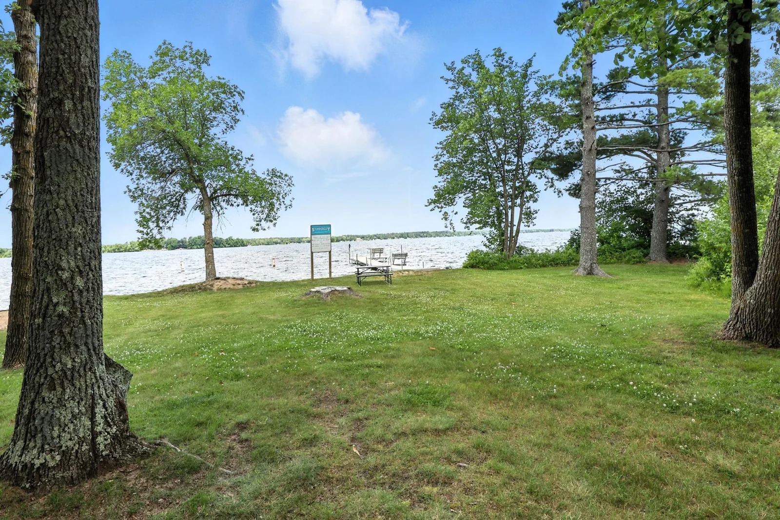 Gently sloping lawn to the lake with a picnic table and clear views of the sandy swimming area—ideal for summer fun.