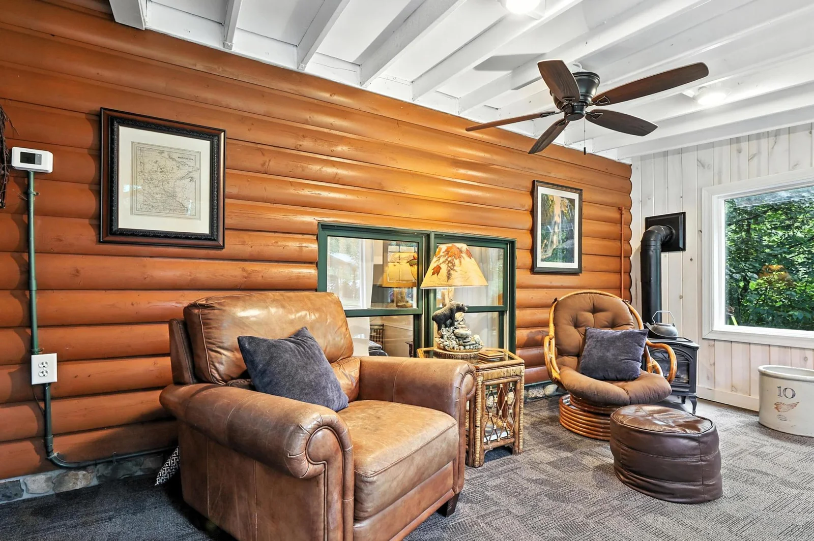 Relax in the comfort of the four-season porch featuring log-style siding, vaulted white beam ceilings, and a cozy mix of leather and rattan seating—ideal for year-round enjoyment.