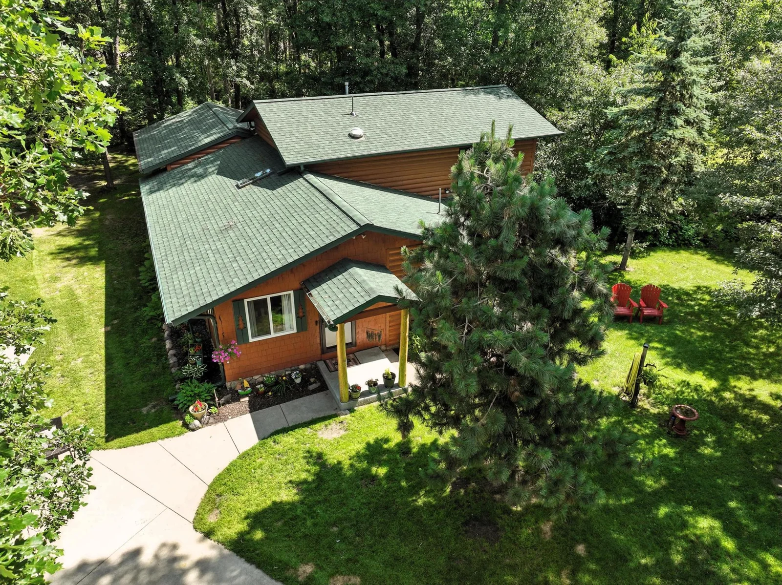 Welcome to your private wooded retreat! This aerial view showcases the home’s charming curb appeal, green shingled roof, and inviting covered entry, all nestled among mature trees on a beautifully landscaped lot.