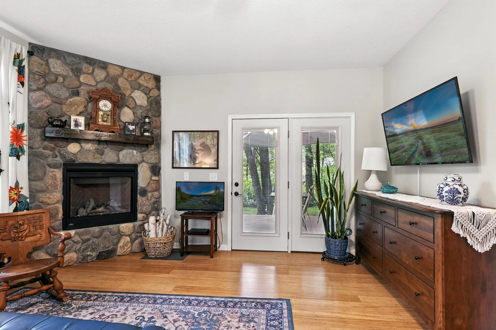 This bedroom combines comfort and function with direct access to a covered patio via glass-paneled French doors, a mounted TV, and a large dresser for storage—all set against rich wood floors and soft neutral walls.