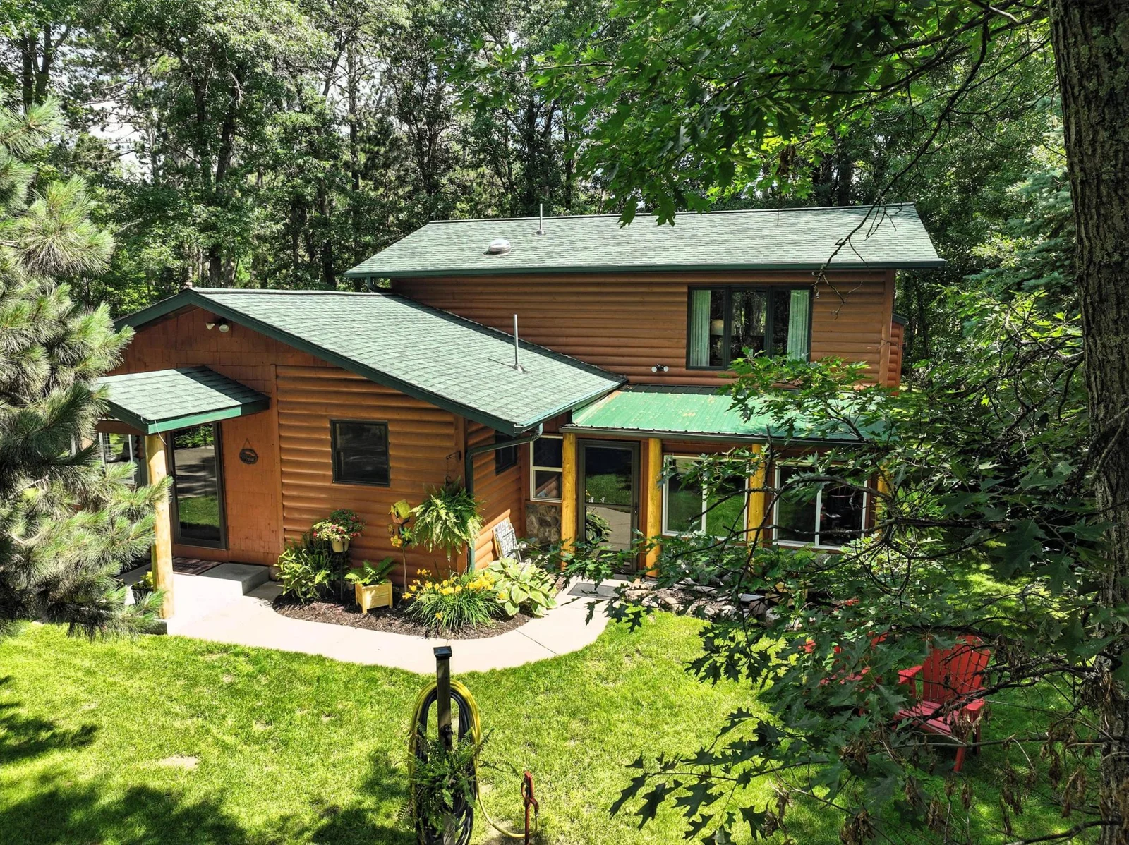 A peaceful backyard oasis framed by forest views, featuring well-maintained landscaping, a concrete walkway, and a cozy area with Adirondack chairs—perfect for evening relaxation.