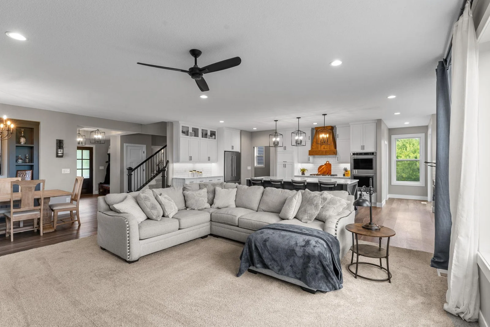 This spacious main-level living room boasts plush carpeting, a ceiling fan, and a cozy gas-burning fireplace with a custom built-ins, all complemented by large windows that fill the space with natural light.