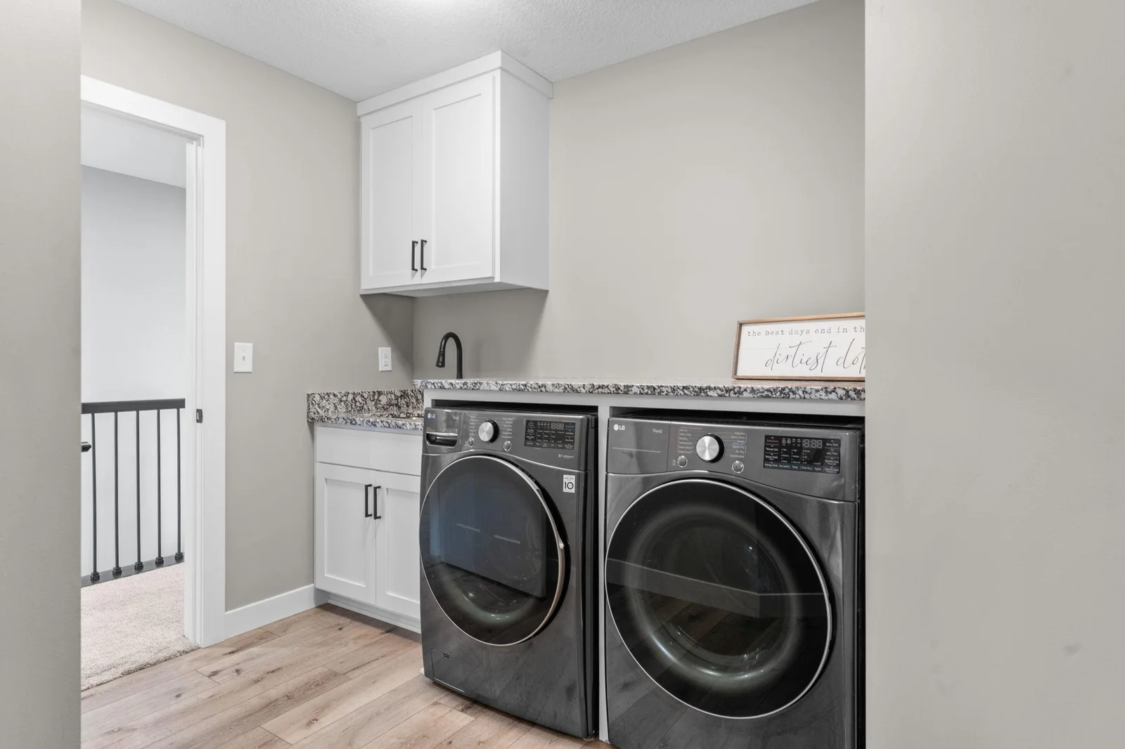 The upper-level laundry room, accessible from both the hallway and the primary bedroom’s walk-in closet, features luxury plank flooring, a sink, ample counter space, and a front-loading LG washer and dryer.