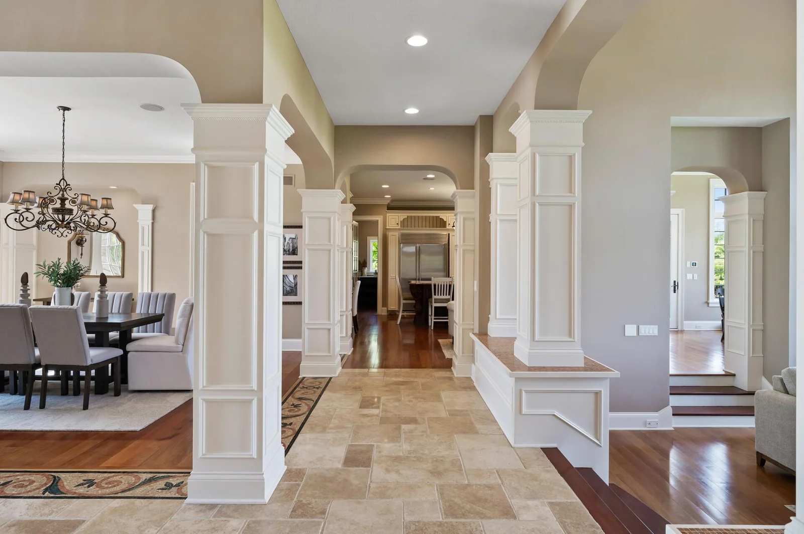 Admire the architectural elements, including the columns and archways, that define the elegant hallway connecting the dining room and other living spaces.