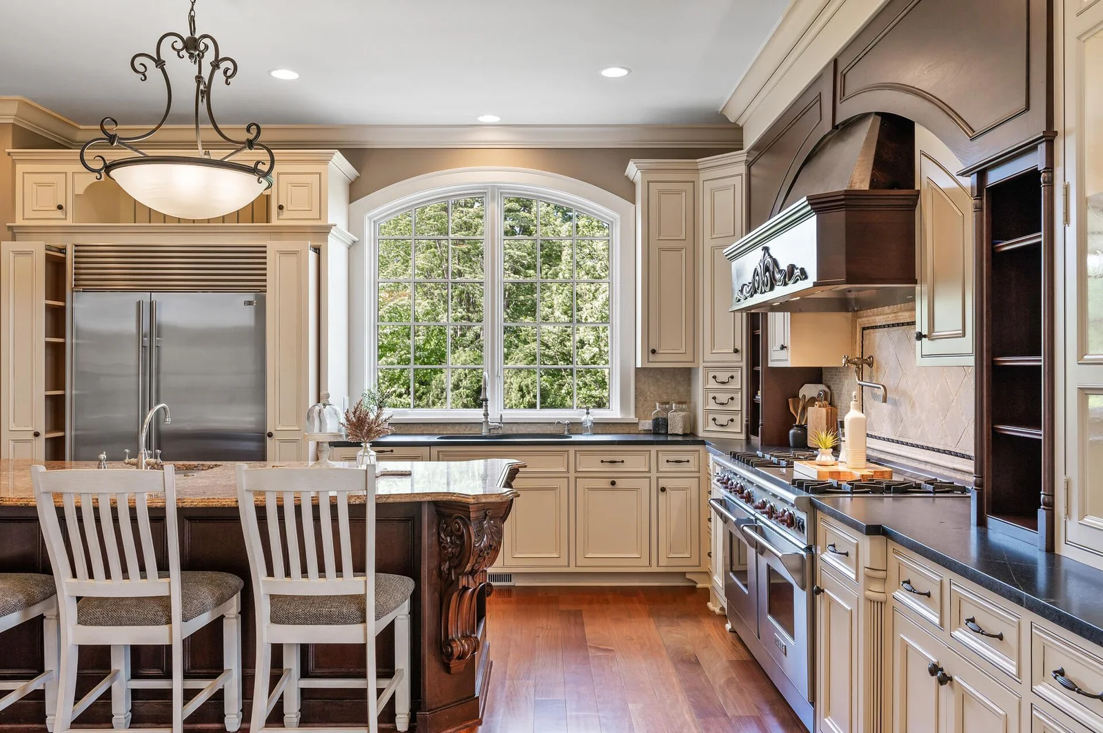 The spacious kitchen island, the abundance of natural light from the arched window, and the integrated Sub-Zero refrigerator are highlights of this culinary space.