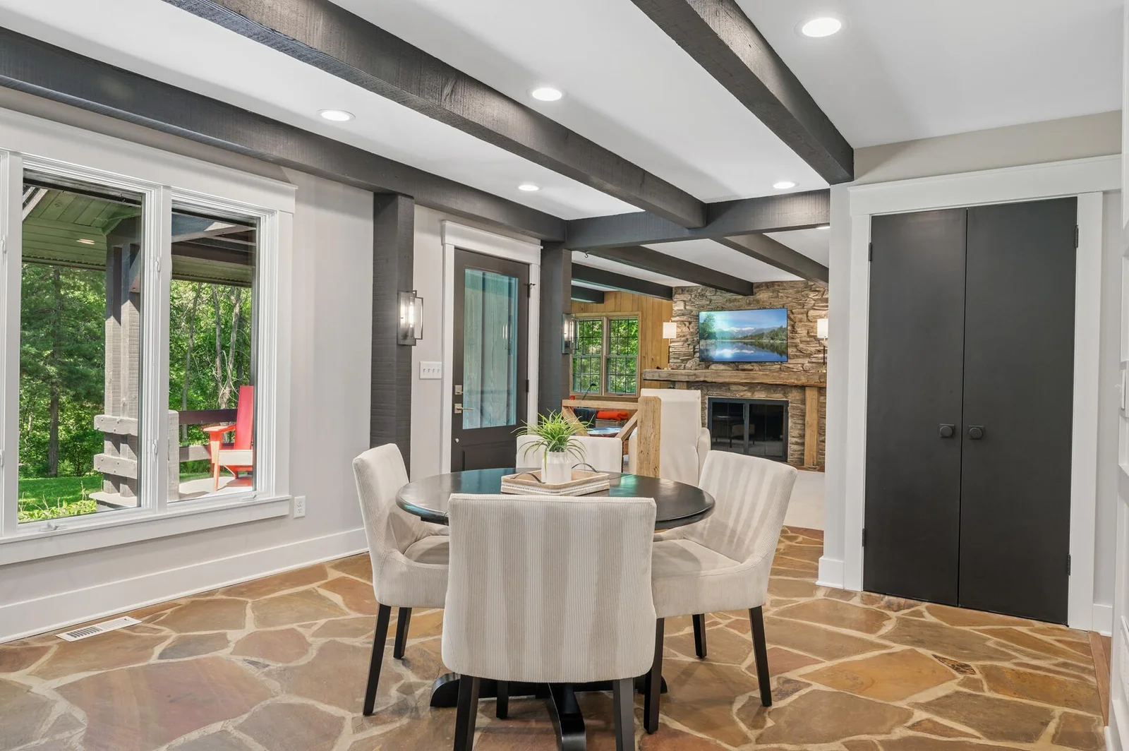 The informal eating area off the kitchen, opens to a large sitting area with walls of windows, wood beam accents, and the original river rock wood fireplace.