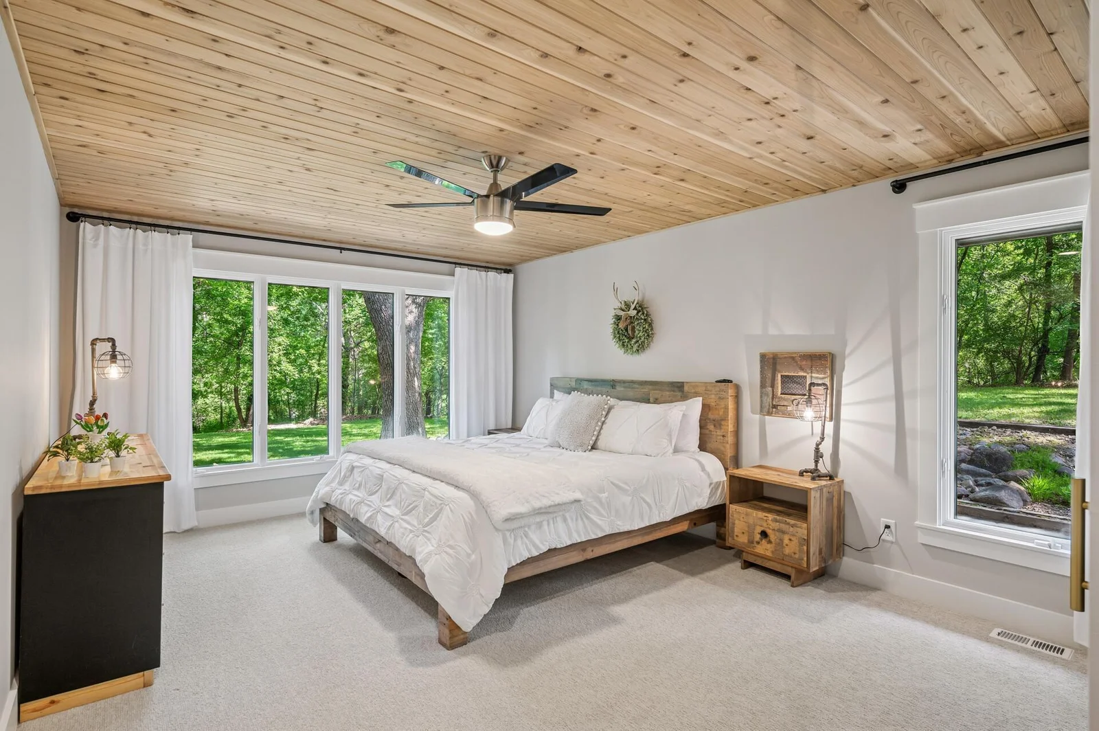 Large owners bedroom on main level has large wall of windows for amazing views of nature accented with warm, wood plank ceiling.