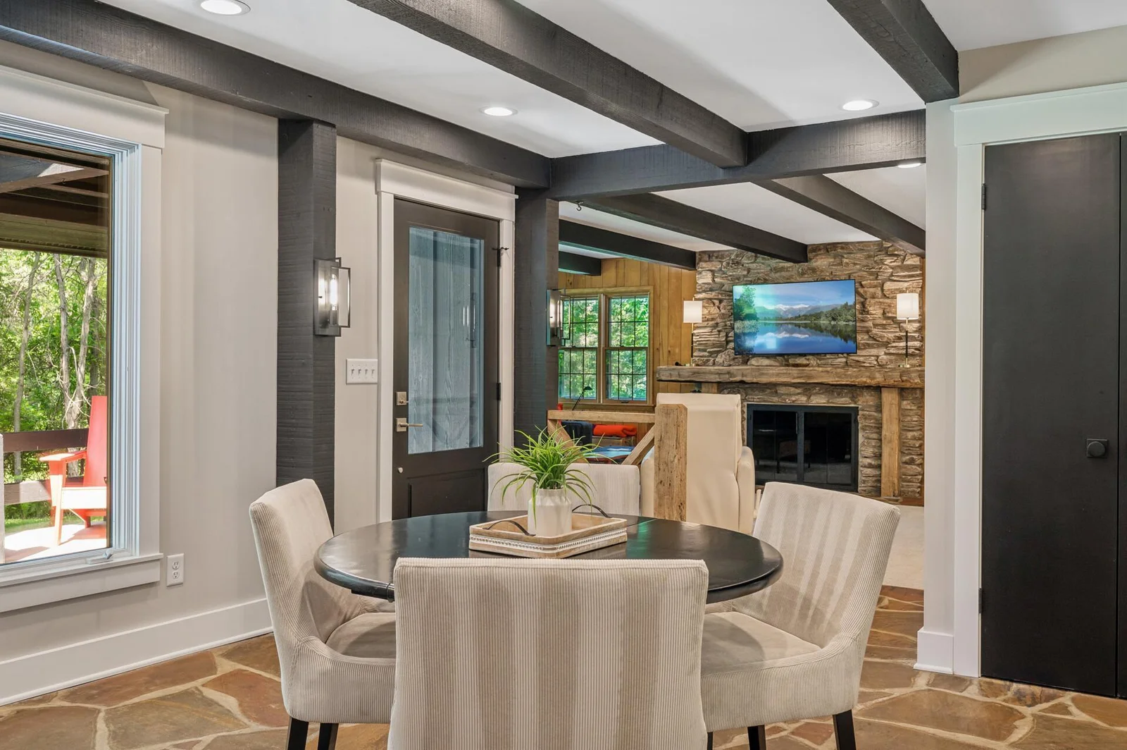 The informal eating area off the kitchen, opens to a large sitting area with walls of windows, wood beam accents, and the original river rock wood fireplace.