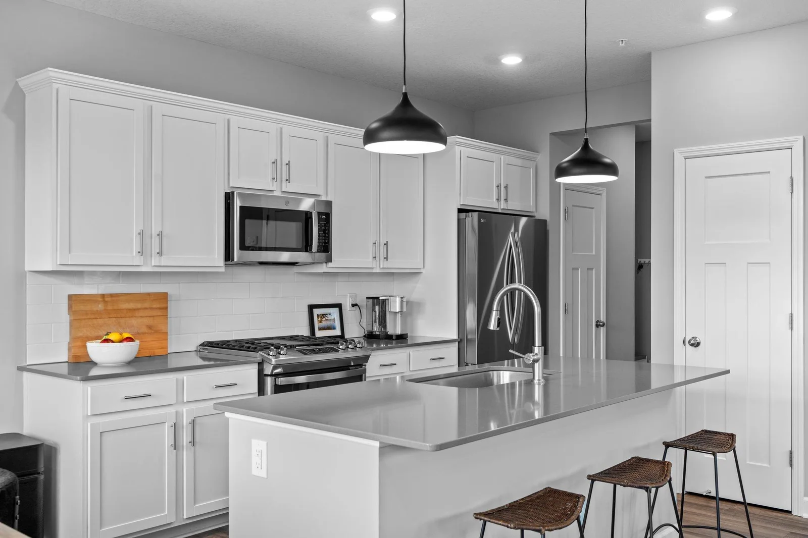 It features abundant white cabinetry, elegant quartz countertops, a sleek tile backsplash, and stainless steel appliances that are just two years old.