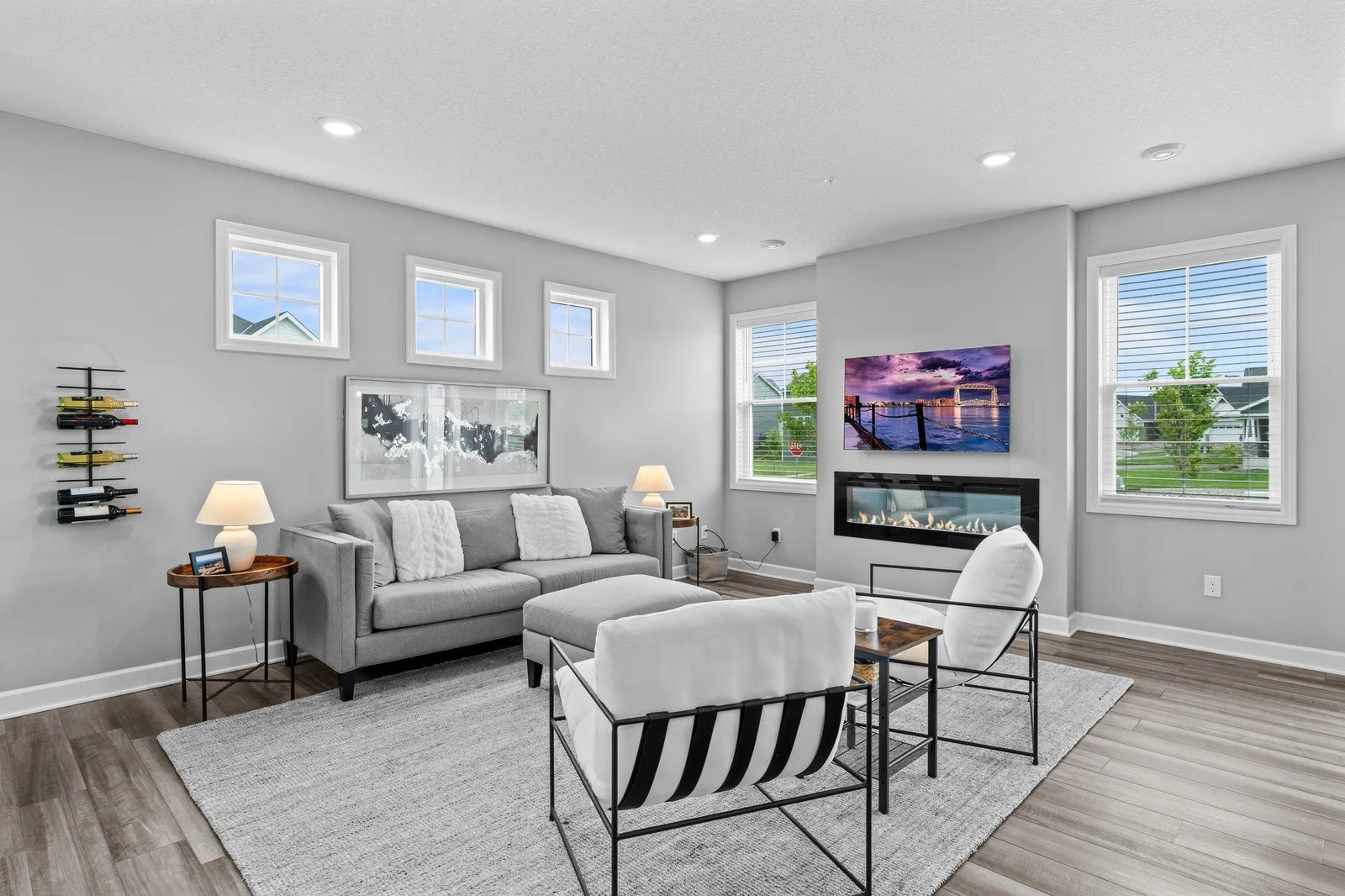 This inviting space features a cozy electric wall-mounted fireplace that adds warmth and ambiance, while an abundance of large windows floods the room with natural light, creating a bright and welcoming atmosphere throughout the day.