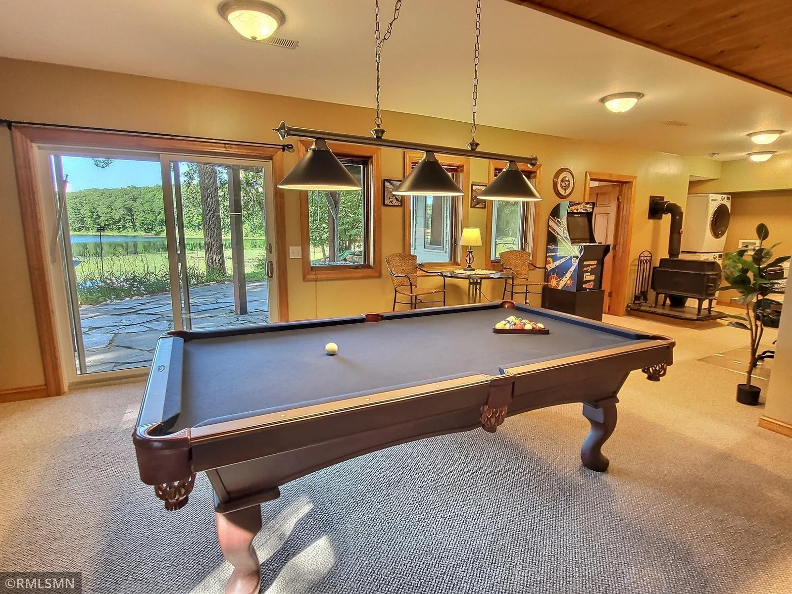 The lower-level great room walks out to a charming stone patio, creating a versatile indoor-outdoor space. Pool table to be included in the sale.