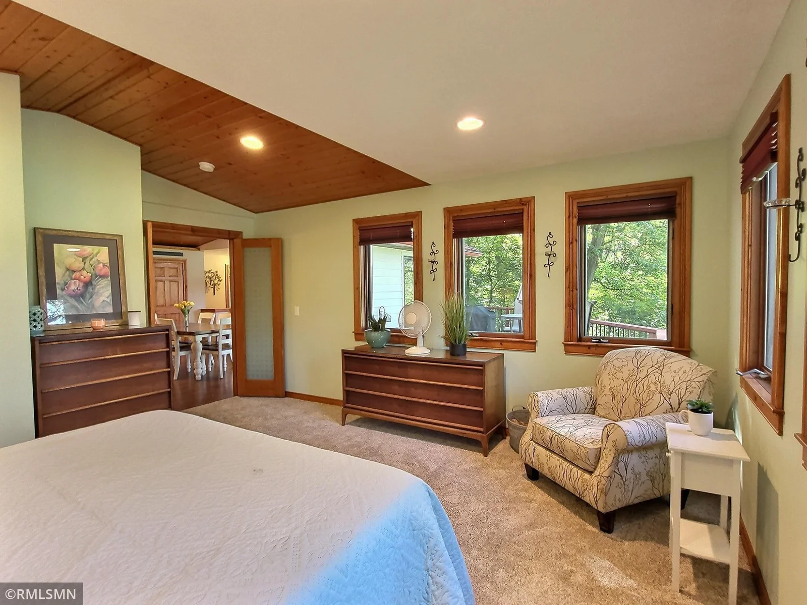 A 2nd shot of the main floor spacious primary bedroom with french doors to the room and the partial natural wood ceiling look.